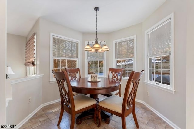 dining space with a chandelier, stone tile floors, and baseboards