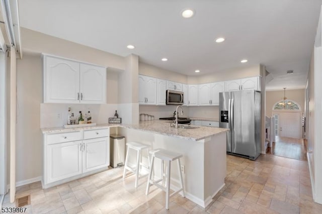 kitchen with light stone counters, stainless steel appliances, a peninsula, white cabinetry, and a kitchen bar