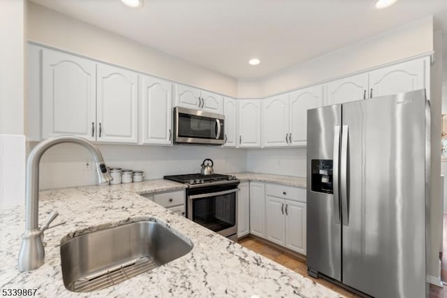 kitchen featuring stainless steel appliances, recessed lighting, white cabinetry, a sink, and light stone countertops