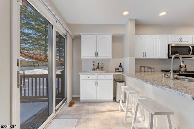 kitchen with white cabinets, light stone counters, stainless steel microwave, a sink, and recessed lighting