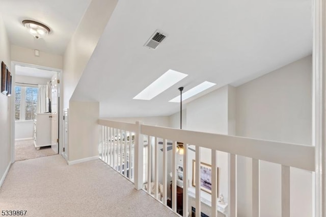 corridor with light carpet, lofted ceiling with skylight, baseboards, and visible vents