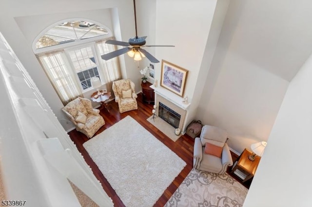 living room with a towering ceiling, wood finished floors, a fireplace with flush hearth, and a ceiling fan