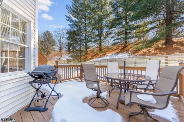 snow covered deck featuring outdoor dining space and a grill