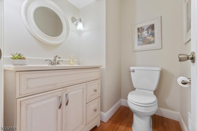 half bath featuring baseboards, vanity, toilet, and wood finished floors