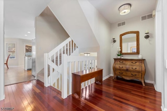 corridor with dark wood-type flooring, visible vents, baseboards, and stairs