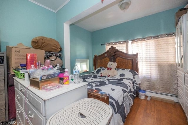 bedroom featuring a baseboard heating unit, ornamental molding, and wood finished floors