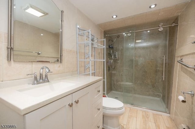 full bath featuring a stall shower, toilet, wood finished floors, vanity, and tile walls