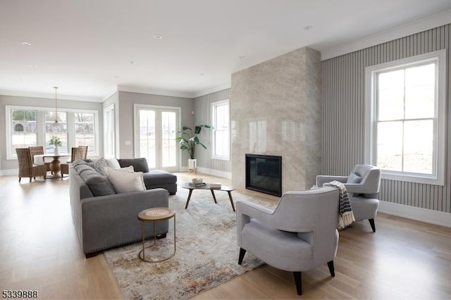 living area featuring light wood-style flooring, a high end fireplace, baseboards, wallpapered walls, and crown molding