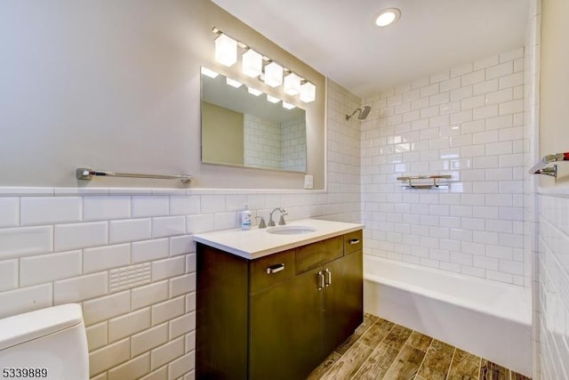 full bath with toilet, bathtub / shower combination, vanity, wood finish floors, and tile walls