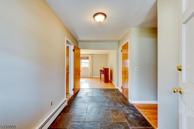 corridor with a baseboard radiator, stone tile flooring, and baseboards