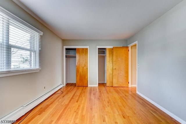 unfurnished bedroom featuring light wood finished floors, a baseboard radiator, baseboards, and two closets