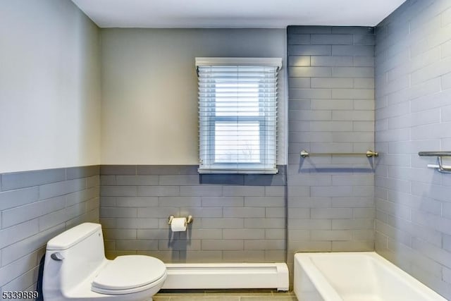 full bath with toilet, a tub to relax in, a baseboard radiator, and tile walls