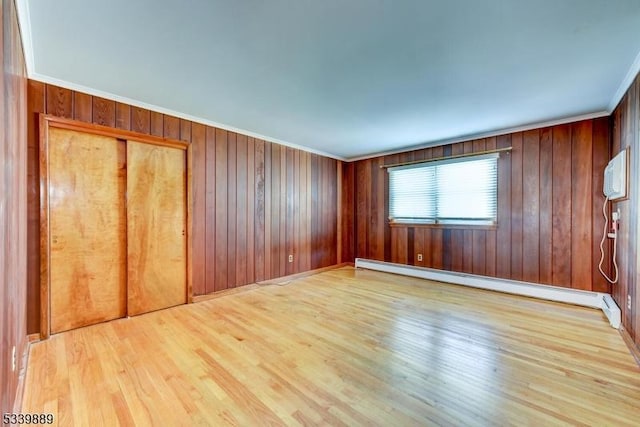 empty room with light wood finished floors, wooden walls, baseboard heating, and crown molding