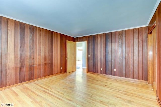 empty room featuring light wood finished floors, wooden walls, and crown molding