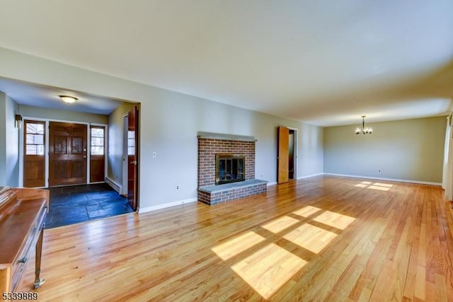 unfurnished living room featuring a brick fireplace, a notable chandelier, baseboards, and wood finished floors