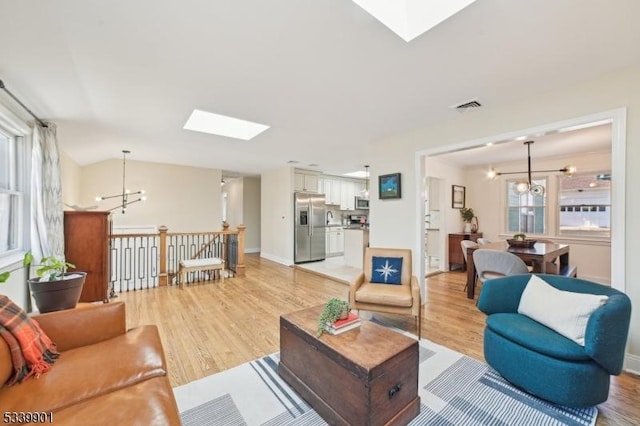 living area featuring an inviting chandelier, light wood-style floors, visible vents, and baseboards