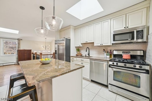 kitchen featuring a sink, light stone counters, stainless steel appliances, a skylight, and decorative backsplash