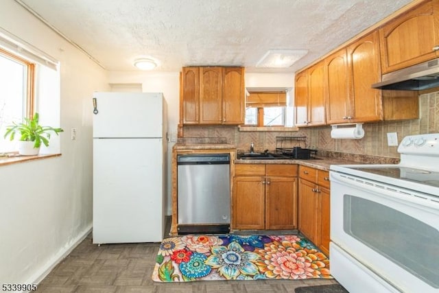 kitchen with white appliances, tasteful backsplash, a textured ceiling, under cabinet range hood, and a sink