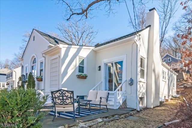 rear view of property featuring entry steps, a patio, an outdoor living space, stucco siding, and a chimney