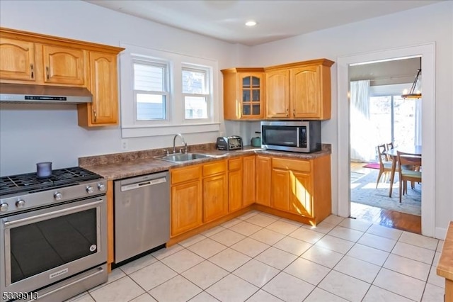 kitchen featuring light tile patterned floors, appliances with stainless steel finishes, glass insert cabinets, a sink, and under cabinet range hood