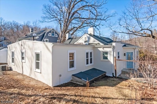 rear view of property with a chimney, central AC, and stucco siding