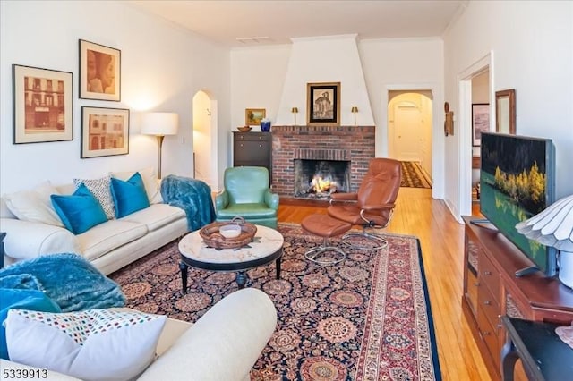 living area with arched walkways, ornamental molding, a brick fireplace, and wood finished floors