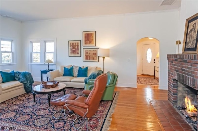 living area with arched walkways, wood finished floors, visible vents, a brick fireplace, and crown molding