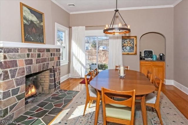 dining room with ornamental molding, a brick fireplace, visible vents, and wood finished floors