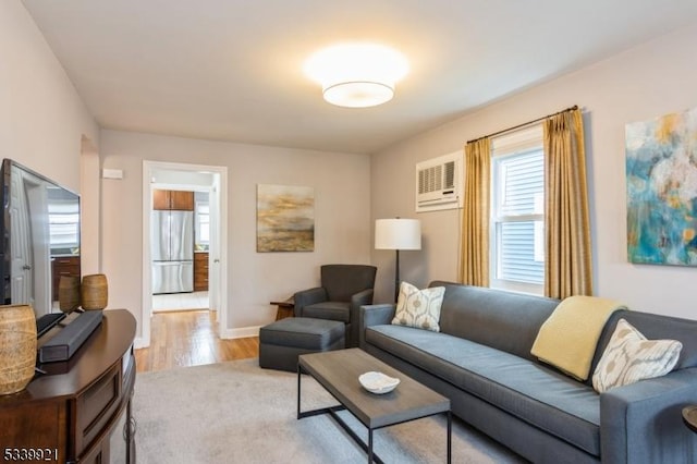 living room with an AC wall unit, baseboards, and light wood finished floors