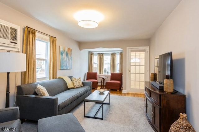 living room with a wall mounted air conditioner, plenty of natural light, and light wood-style flooring