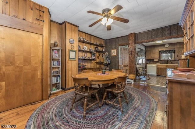 dining area with wood walls, wood-type flooring, and a ceiling fan