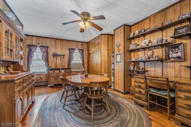 dining room with a baseboard heating unit, dark wood-type flooring, wood walls, and a ceiling fan