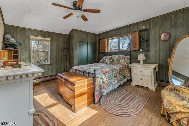 bedroom featuring multiple windows, ceiling fan, baseboard heating, and wood finished floors