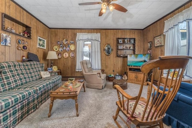 carpeted living area with ceiling fan, wood walls, and crown molding