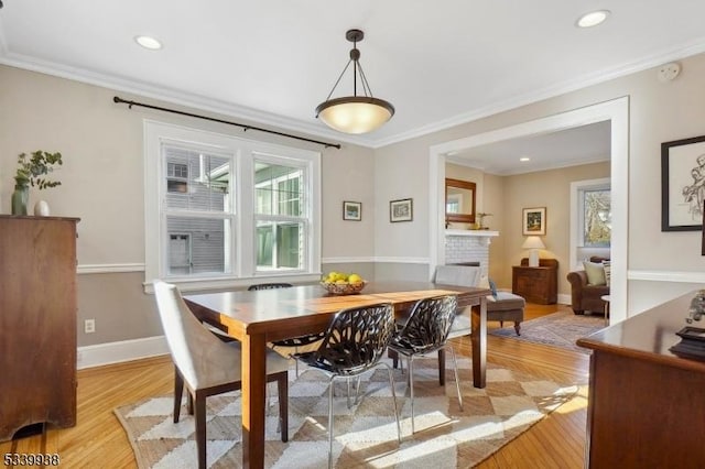 dining space with crown molding, a brick fireplace, plenty of natural light, and light wood-style flooring