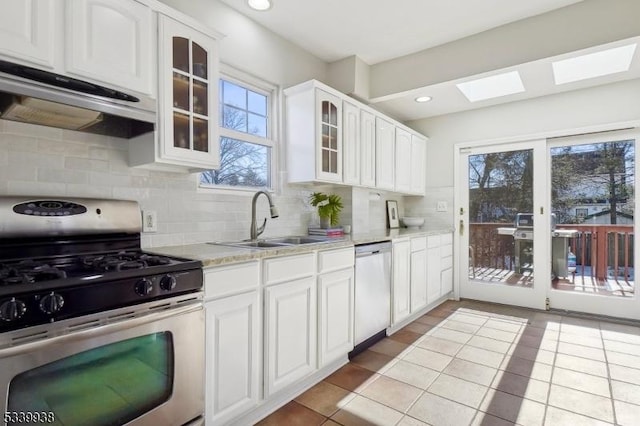 kitchen featuring stainless steel appliances, glass insert cabinets, white cabinetry, a sink, and under cabinet range hood