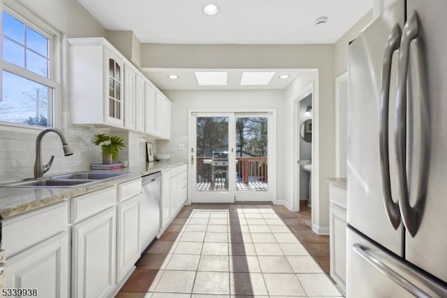 kitchen with a skylight, appliances with stainless steel finishes, glass insert cabinets, white cabinetry, and a sink