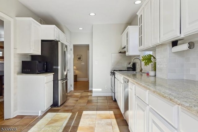 kitchen with light stone counters, light tile patterned flooring, stainless steel appliances, white cabinetry, and glass insert cabinets