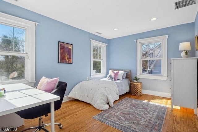 bedroom with wood finished floors, visible vents, and multiple windows