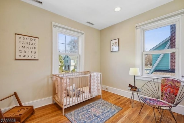 bedroom with baseboards, multiple windows, visible vents, and wood finished floors