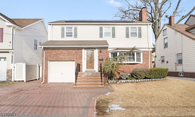 view of front facade featuring decorative driveway, brick siding, roof mounted solar panels, and an attached garage