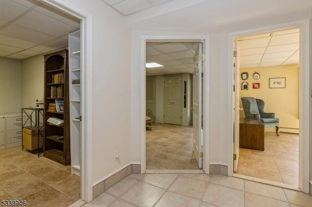 hallway featuring a paneled ceiling, light tile patterned floors, and baseboards