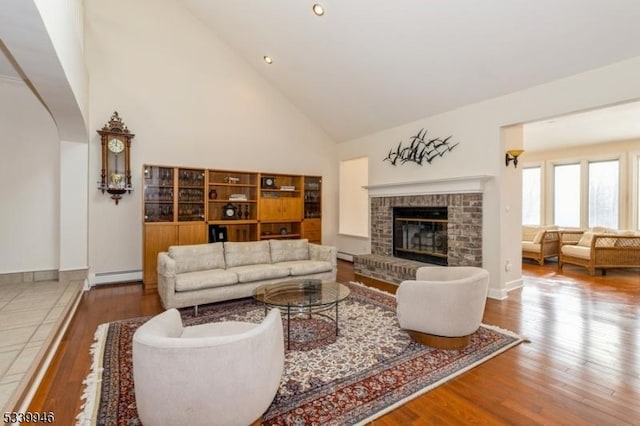 living room featuring a baseboard radiator, a fireplace, high vaulted ceiling, and wood finished floors