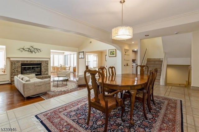 dining room with ornamental molding, lofted ceiling, a brick fireplace, and stairs