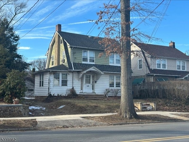 colonial inspired home featuring roof with shingles, a chimney, fence, and a gambrel roof