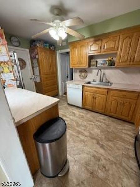 kitchen featuring white dishwasher, a sink, a ceiling fan, light countertops, and brown cabinetry