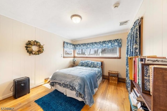 bedroom with a baseboard heating unit, wood finished floors, and visible vents