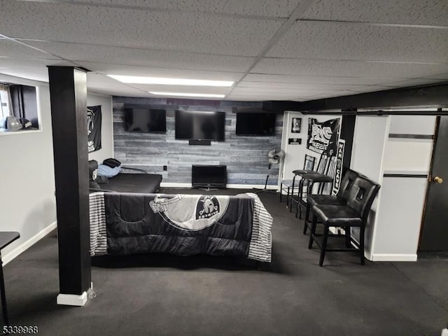 interior space with a paneled ceiling, a dark floor, baseboards, and a barn door