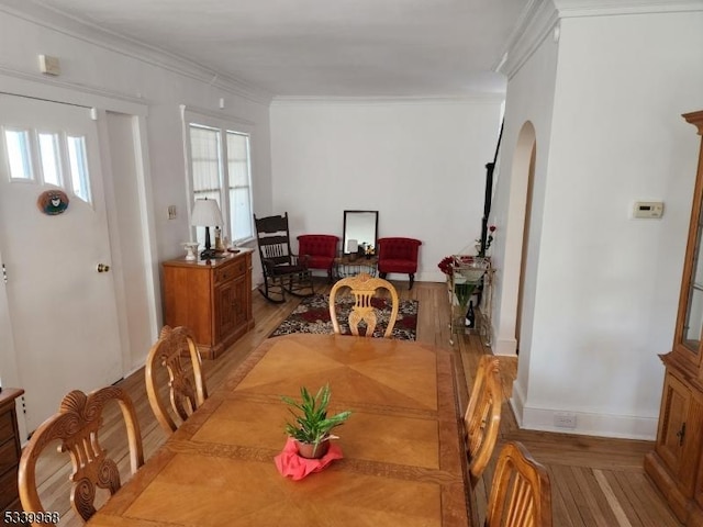 dining room with light wood-type flooring, a healthy amount of sunlight, crown molding, and arched walkways