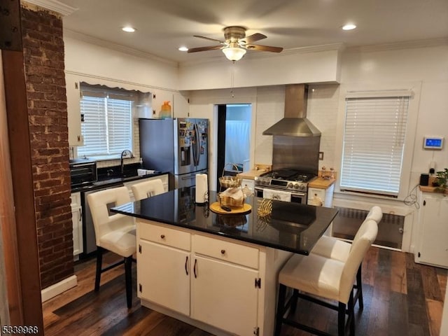 kitchen with wall chimney exhaust hood, stainless steel appliances, white cabinets, a kitchen island, and a kitchen breakfast bar